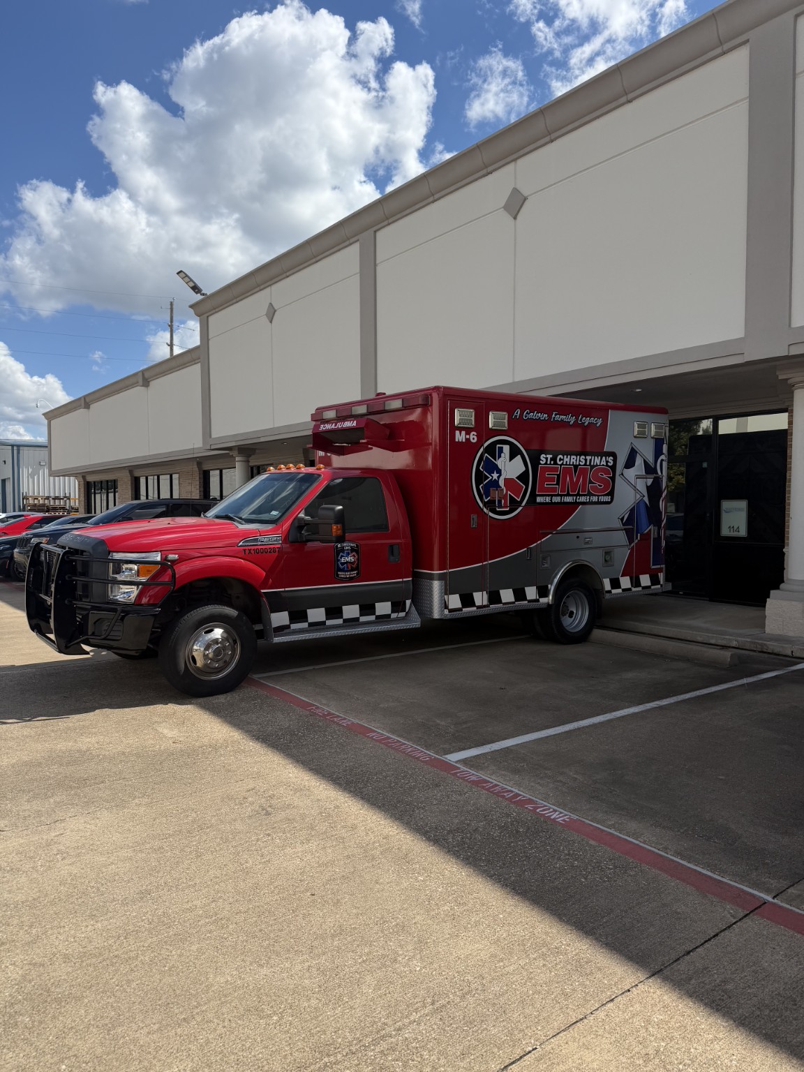 Red St. Christina’s EMS M-6 ambulance parked outside a building, displaying the company name and Where Our Family Cares For Yours motto